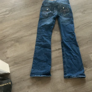 Blå bootcut jeans med broderi - Säljer ett par blå jeans med bootcut passform. Baktill finns snygga broderade detaljer och bling på fickorna som ger extra stilpoäng. Klassisk femficksmodell med knapp och dragkedja framtill. Perfekt för dig som gillar lite utsvängda ben och coola detaljer. Priset kan diskuteras. OPS 59 kr för frakten 