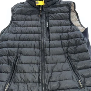 Äkta svart dunväst från Parajumpers - Snygg svart dunväst från Parajumpers med quiltad design och gul detalj vid kragen. Västen har dragkedja framtill, tre fickor med dragkedja och en grå insida. 