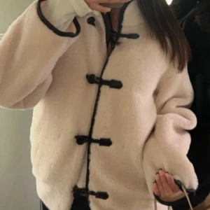 Vit/beige teddy jacka - Säljer en beige/vit jacka med svarta kantband och coola knytknappar framtill. Jackan är storlek xxs men sitter som en s vilket är typiskt för dessa jackor (att vara större). Kan gå ner i pris vid snabb affär - stor efterfrågan på denna jacka