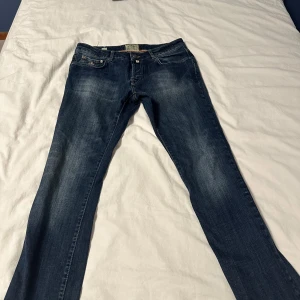 Morris mörkblå straight jeans 33/34 - Snygga mörkblå jeans från Morris med klassisk femficksdesign och guldfärgad broderad logga på myntfickan. Jeansen har raka ben, kontrastsömmar och en vintage tvättad look. Materialet är slitstark denim i bomull. Perfekt för dig som gillar stilrena och tidlösa jeans.
