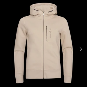 Beige hoodie från Sail Racing - Snygg beige hoodie från Sail Racing med hel dragkedja och huva med snörning. Tröjan har en bröstficka med dragkedja och diskret logga på vänster sida. Storlek L i barn men passar M/S