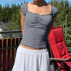 Randig croppad topp med volangkant - Säljer en blåvit randig topp från hollister med söt volangkant runt halsringningen och ärmsluten. Toppen har en lätt rynkad detalj framtill och kan bäras både med axlarna uppe eller offshoulder. Materialet är ribbad bomull som är mjukt och skönt mot kroppen. Säljer även kjolen💓