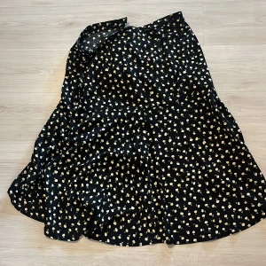 Svart blommig långkjol från Lindex - Flowig svart långkjol från Lindex med sött blommigt mönster i gult och vitt. Kjolen har en lätt utsvängd form och känns riktigt skön och luftig. Perfekt för dig som gillar en feminin och chill stil.