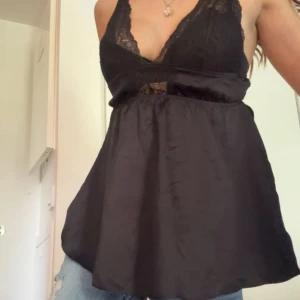 Victoria secret spetslinne - Supersnygg svart linnetopp från Victorias secret med spetsdetaljer och djup v-ringning. Toppen har tunna axelband. Storlek XS. Satin material.
