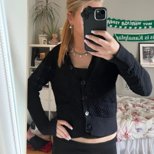 Svart stickad kofta med knappar - Säljer en svart stickad kofta med coolt strukturmönster och fyra stora knappar framtill. Koftan har två fickor och långärmade ärmar. Passar dig som gillar en chill och enkel stil med lite edge. Perfekt att slänga över en topp för extra lager. säljer för den är lite för liten❣️