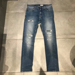 Tiger Of Sweden Jeans - Säljer ett par snygga blå jeans från T/J med coola slitningar på framsidan. Skick || 9/10, ytterbenslängd: 101 || inerbenslängd: 79 || midja: 40. Perfekta för en avslappnad stil. Slim fit.