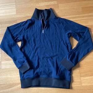 Marinblå half zip tröja Selected Homme - Snygg marinblå långärmad tröja från Selected Homme i storlek M. Tröjan har en hög krage med half zip-dragkedja och svarta ribbade muddar vid ärmslut och nederkant. Perfekt för chill dagar och enkel att matcha med jeans eller joggers.