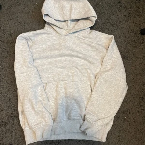 Ljusgrå hoodie från Jack & Jones - Säljer en stilren ljusgrå hoodie från Jack & Jones. Tröjan har en klassisk huva, stor magficka och ribbade muddar vid ärmslut och nederkant. Perfekt för chill dagar och enkel att matcha med jeans eller joggers. Materialet är mjuk bomull för skön komfort.