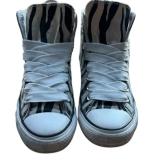 Custom Converse Fat Laces Zebra - Snygga Converse high top sneakers med svart och vit zebramönster. Skorna har klassisk rund tå, vit platt sula och vita snören. Tillverkade i bomullscanvas med Converse All Star-logga på sidan. Perfekt för dig som vill sticka ut med coola detaljer.Storlek 40-41,finns en skada inyti skorna så be om bilder för den,Custom skor