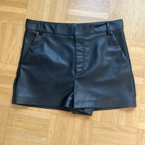 Svarta skinnshorts - Snygga svarta shorts i skinnimitation och klassisk passform. De har bälteshällor, fickor fram och en stilren look som passar till många olika outfits. Materialet är mjukt och ger en cool vibe, perfekt för dig som gillar att sticka ut. Skriv vid minsta fråga!💕💕