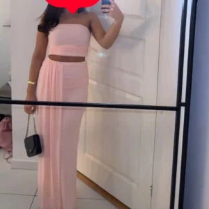 Ljusrosa kjol och topp - Säljer en superfin ljusrosa kjol set med omlott-design och axelbandslös överdel. Settet har en croppad topp och ett långt, flowy kjolparti som ger en elegant siluett. Perfekt för sommarens alla tillfällen! Matcha med smycken och väska för en komplett look.