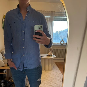 Blå linneskjorta från Morris - Snygg blå skjorta från Morris i 100% linne, perfekt för dig som gillar stilrena och klassiska plagg. Skjortan har lång ärm, knappar framtill och en liten broderad logga på bröstet. Passformen är normal och materialet känns lätt och luftigt.