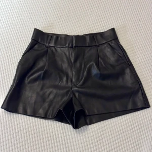 Svarta skinnshorts från Zara - Säljer dessa snygga skinn imitation shorts från Zara. De har bälteshällor med fickor på framsidan ochfejk fickor på baksidan. De har även en metallhake och dragkedja för att spänna åt✌🏼