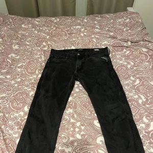 Svarta Replay Anbass jeans - Säljer ett par svarta Replay Anbass jeans med klassisk femficksdesign och snygga detaljer vid fickorna. Jeansen har en slim passform och är tillverkade i mjukt jeanstyg med lite stretch för extra komfort. Perfekta för dig som gillar stilrena och moderna jeans.