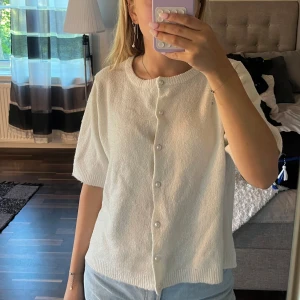 Vit kofta med pärlknappar från 157 - Säljer en söt vit kofta från 157 med korta ärmar och rund hals. Koftan har pärlknappar hela vägen framtill och är stickad i ett mjukt material. Perfekt att slänga på över en topp eller linne🤍🤍