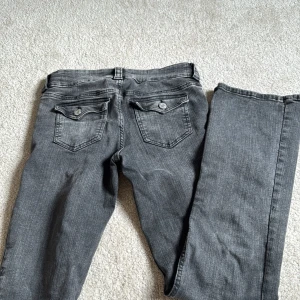 Bootcut grå jeans från H&M - Snygga grå jeans från H&M med bootcut-ben och låg midja. Jeansen har justerbar midja och coola bakfickor med lock och knappdetalj. Materialet är mjukt jeans-tyg med lätt tvättad look. Perfekt för dig som gillar avslappnad stil med lite edge.               Pris går att diskutera💞