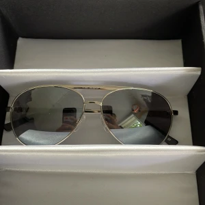 Silvriga aviator-solglasögon från vonzipper Ny pris 1200 - Snygga aviator-solglasögon från vonzipper  med silvrig metallram och svarta skalmar. Glasen är mörka och har en klassisk pilotform som ger en cool vibe. Perfekt för dig som vill ha en stilren och tidlös look. Säljes i originalask.