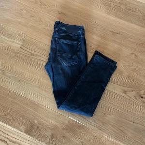 Replay Anbass jeans mörkblå herr - Säljer ett par Replay Anbass jeans i mörkblå tvätt med snyggt slitna detaljer. Modellen har smal passform och klassisk femficksdesign. Jeansen är tillverkade i stretchig bomull för extra komfort och har Replay-logga på fickan.