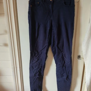 Mörkblå jeans - Ett par mörkblå jeans med slim passform och broms/guld färgade knappar. Byxorna har en smal och tajt siluett och har en midrise midja. Materialet är lite tunnare än vanligt jeanstyg så de går att använda när det är lite varmare ute. På etiketten står det att storleken är 36 men jag skulle säga att de passar mer som storlek 34 eller en XS. På bilden ser de väldigt skrynkliga ut men det är bara för att de har legat i en påse garderoben ett tag.