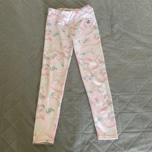 Blommiga leggings från Iconic -  Supersnygga leggings från Iconic (Stadium) i ljusrosa med blommigt mönster och gröna blad. Stretchiga och sitter tight – perfekta både för träning, dans eller chill.  Materialet är mjukt och följsamt, vilket gör dem riktigt bekväma att ha på sig. Nästan oanvända – bara testade ett par gånger, i toppskick! Storlek: Barn 134/140