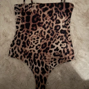 Leopardmönstrad bodysuit med smala band - Snygg leopardmönstrad bodysuit med smala axelband. Tight passform och högt skuren i benen, perfekt för att sticka ut. Mjukt och stretchigt material som sitter bekvämt mot kroppen. Aldrig använd