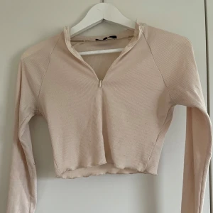 Beige ribbad magtröja långärmad - Säljer en beige croppad långärmad topp med ribbad struktur och liten dragkedja framtill. Toppen har slits vid ärmsluten och en lätt vågig kant nertill. Kan skicka fler bilder vid intresse!☺️