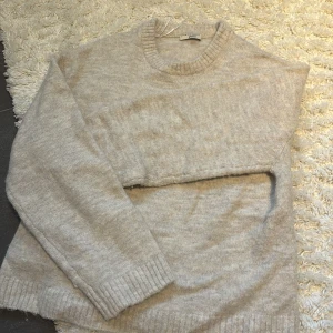 Beige stickad tröja från Gina Tricot - Mysig beige stickad tröja från Gina Tricot med rund halsringning och ribbade muddar vid ärmslut och nederkant. Perfekt för lager-på-lager och enkel att matcha med jeans eller kjol. Snygg basic som funkar året runt. Inte alls mycket använd och i bra skick💕