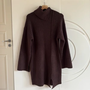 Ida Carlsson * NAKD Brun stickad klänning  - Mysig brun stickad klänning med lång ärm. Klänningen har en hög krage och en snygg slits nertill framtill, vilket ger en cool och avslappnad vibe. Storlekslappen är avklippt.