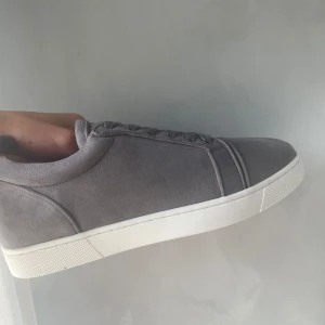 Gråa louboutin skor - Stilrena sneakers i grå mocka med vit sula och cool röd undersida. Skorna har klassisk snörning och en minimalistisk design som passar till det mesta. Perfekta för dig som gillar en clean look med en twist.