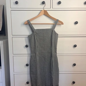 Svartvit rutig kortklänning - Snygg svartvit kortklänning med rutigt mönster och breda axelband. Klänningen har en figurnära passform och raka linjer, perfekt för dig som gillar en stilren look. Passar lika bra till sneakers som till klackar.