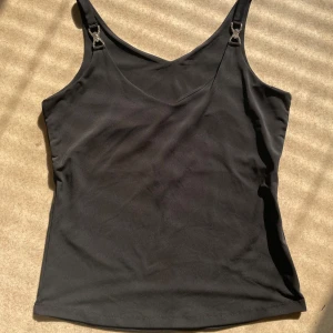 Svart linnetopp med strassdetaljer, H&M - Svart linnetopp från H&M i slät polyester med smala axelband och snygga strassdetaljer framtill. Toppen har en enkel, figurnära passform.