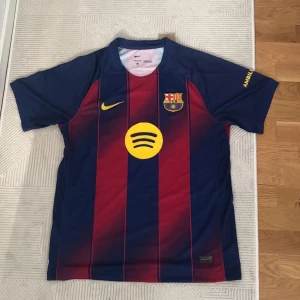 FC Barcelona Raphinha 11 Nike tröja - Säljer en  FC Barcelona matchtröja med Raphinha 11 på ryggen. Tröjan är blå och röd med gula detaljer, klubbmärke och sponsorloggor. Klassisk randig design i lätt och ventilerande material, perfekt för dig som älskar Barca.