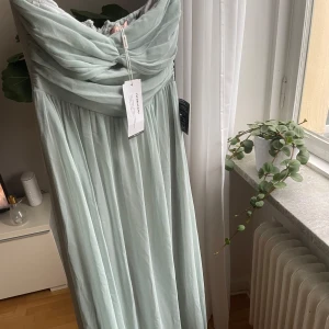 Ljusgrön axelbandslös långklänning NLY Eve - Festlig ljusgrön långklänning från NLY Eve med axelbandslös design och draperad överdel. Klänningen har en flowy kjol och stängs med dragkedja i ryggen. Perfekt för bal och bröllop! Materialet känns lätt och elegant. Aldrig använd, lappar kvar