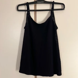 Svart linnetopp från KappAhl - En svart linnetopp från KappAhl med smala axelband och snyggt korsade band i ryggen. Toppen är tillverkad i en mjuk blandning av viskos och polyester, vilket gör den både lätt och bekväm. Perfekt att styla med jeans eller kjol för en enkel look. Etiketten för storleken finns inte kvar men den är storlek s måtten kan självklart fås vid intresse 