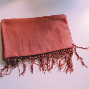 Glittrig korall halsduk med fransar - Snygg korall halsduk med glittriga detaljer och långa fransar i ändarna. Perfekt accessoar för att lyfta din outfit med lite extra shimmer. Mjuk och lätt att styla på olika sätt.  Tråddragningar, obehandlade fläckar & noppror annars helt skick