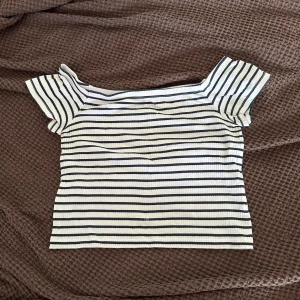 Randig offshoulder topp  - Superfin offshoulder topp från H&M Divided i vitt med svarta ränder. Kortärmad och figurnära passform, perfekt till jeans eller kjol. Mjuk och stretchig bomullskvalitet som känns skön mot huden.