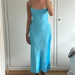 Ljusblå långklänning från Asos - Supersnygg ljusblå långklänning från AsYou med tunna axelband, öppen rygg med snörning och hög slits på sidan. Klänningen är figurnära och gjord i glansig polyester som ger en lyxig känsla. Perfekt för dig som vill sticka ut!