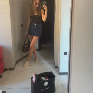 Mörkblå jeanskjol med fickor - Snygg mörkblå jeanskjol med klassiska fickor fram och bak, samt knapp och dragkedja i midjan. Kjolen har en rak, kort passform och passar perfekt till en trendig vardagslook.