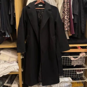 Svart kappa från Gina Tricot XS - Snygg svart kappa från Gina Tricot i storlek XS. Klassiska modell med bred krage, knytskärp i midjan. Lång och varm. Använd en sesong nypris 799kr