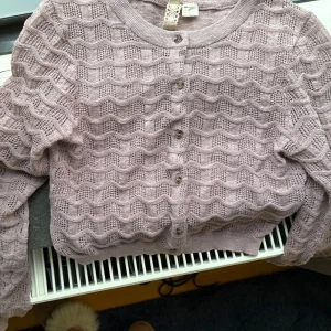 Hålstickad kofta  - Superfin lila hålstickad kofta med vågigt mönster och knappar framtill. Koftan har rund halsringning och långa ärmar. 