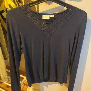 Mörkblå långärmad topp med spets - Supersnygg mörkblå långärmad topp från Gina Tricot med v-ringning och fina spetsdetaljer runt halsen. Säljer då den ej kommer till användning!