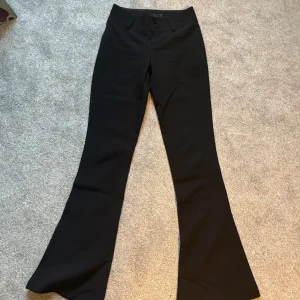 Svarta bootcut-byxor Gina Tricot XXS - Snygga svarta bootcut kostymbyxor från Gina Tricot i storlek XXS. Byxorna har medel midja, klassisk knappstängning och bälteshällor. De är i ett stretchigt material som sitter skönt och har en riktigt clean look med utsvängda ben.
