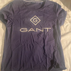 Mörkblå GANT t-shirt med logga - Snygg mörkblå t-shirt från GANT med klassisk vit logga framtill. T-shirten har rund halsringning och korta ärmar. Tillverkad i mjuk bomull som är skön mot huden. Perfekt för en clean och stilren look.