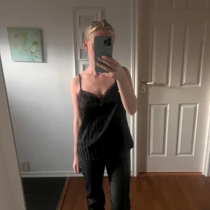 Svarta skinnbyxor med rak passform - Säljer ett par svarta skinnbyxor med klassisk rak passform och midja som sitter precis under naveln. Byxorna har en stilren look med fickor fram och knappstängning. Perfekta för dig som vill ha en edgy vibe till din outfit.