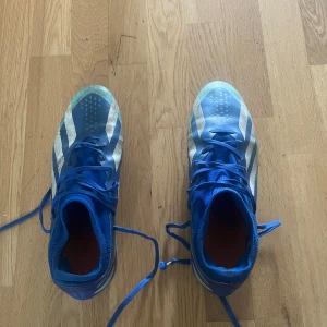Blå adidas Crazyfast fotbollsskor elite - Säljer ett par blå adidas Crazyfast fotbollsskor med vita ränder och snörning. Skorna har en smal passform, rund tå och platt sula med dobbar för bra grepp på planen. Ovandelen är i syntetmaterial och designen är sportig och modern.