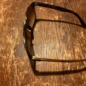 Ray-Ban bruna solglasögon - Snygga solglasögon från Ray-Ban med bruna, fyrkantiga bågar och tonade linser. Klassisk modell med transparent brun plast och diskret logga på skalmen. Perfekta för att lyfta din stil under soliga dagar.