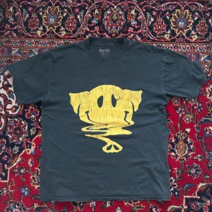 Cypress Hill t-shirt med smileytryck - Svart loose fit t-shirt från Cypress Hill med stort gult smileytryck på framsidan och texten 'Cypress Hill Elephants on Acid' på ryggen. Klassisk rund hals och korta ärmar. Perfekt för dig som gillar bandmerch och streetstyle.
