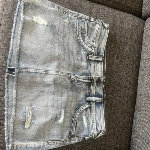 Ljusblå jeanskjol från Express Jeans - Säljer en ljusblå jeanskjol från Express Jeans med slitna detaljer och fransad nederkant. Kjolen har klassiska fickor fram och bak samt bälteshällor. Perfekt för dig som gillar en avslappnad och trendig stil. Köpt i Polen! Nypris var runt 300