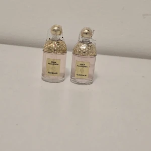 Guerlain Aqua Allegoria parfym - Två små flaskor Guerlain Aqua Allegoria parfym med ljusrosa vätska. Flaskorna är genomskinliga med guldig bikakemönstrad kork och rund topp. Snygg och lyxig design som känns exklusiv och elegant.