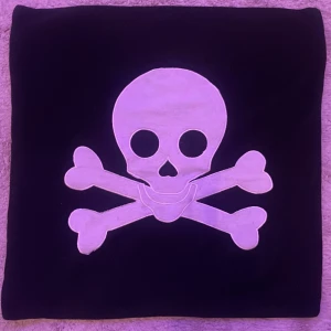 Svart kuddfodral med dödskalletryck - Coolt svart kuddfodral med stort vitt dödskalle- och korsade ben-motiv på framsidan. Köpte den på secondhand men är tvättad många gånger utan användning💖